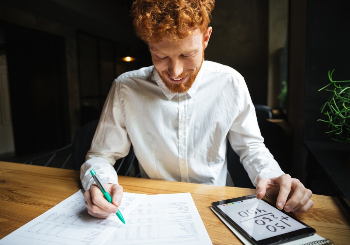 Man reviewing documents with a tablet and pen at a desk.