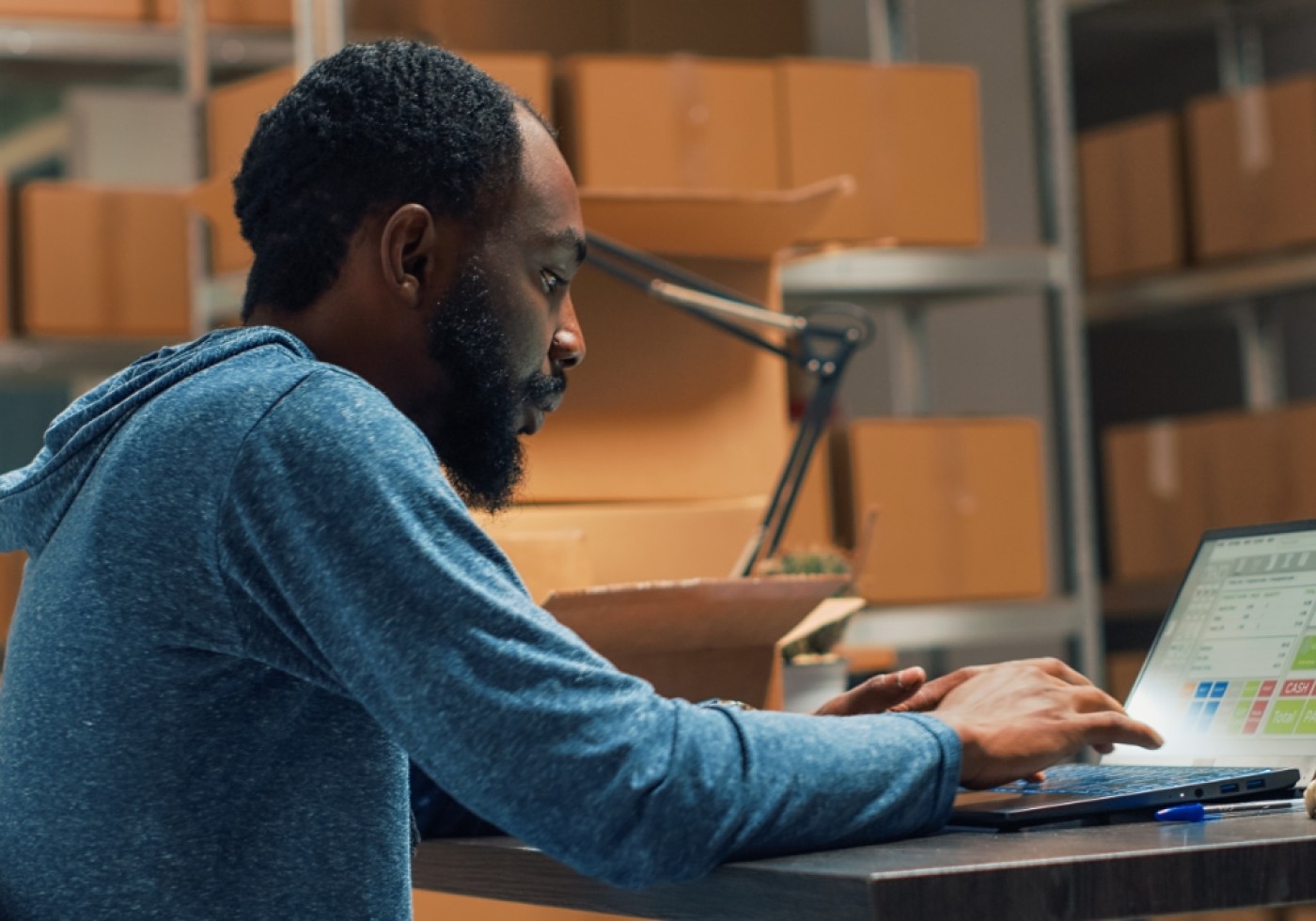 Man working on a laptop in a storage room with boxes in the background
