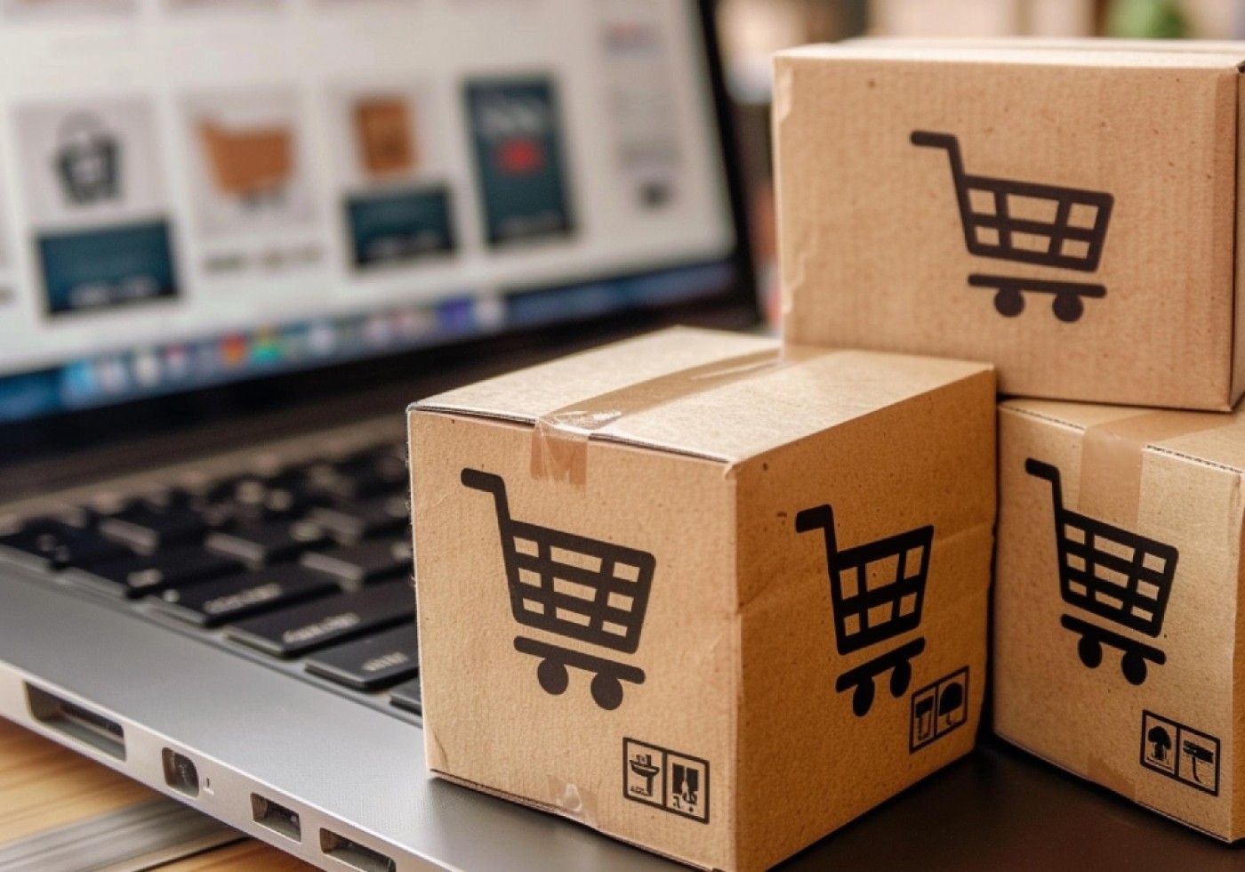Small cardboard boxes with shopping cart icons beside a laptop displaying e-commerce website.
