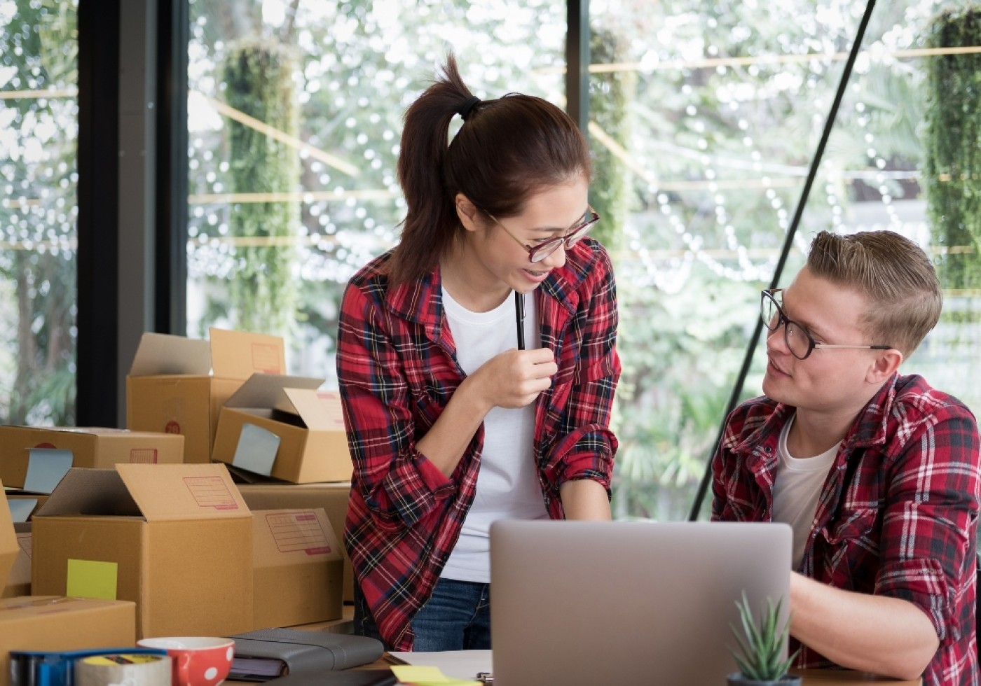 Two colleagues discussing work at a table surrounded by cardboard boxes.