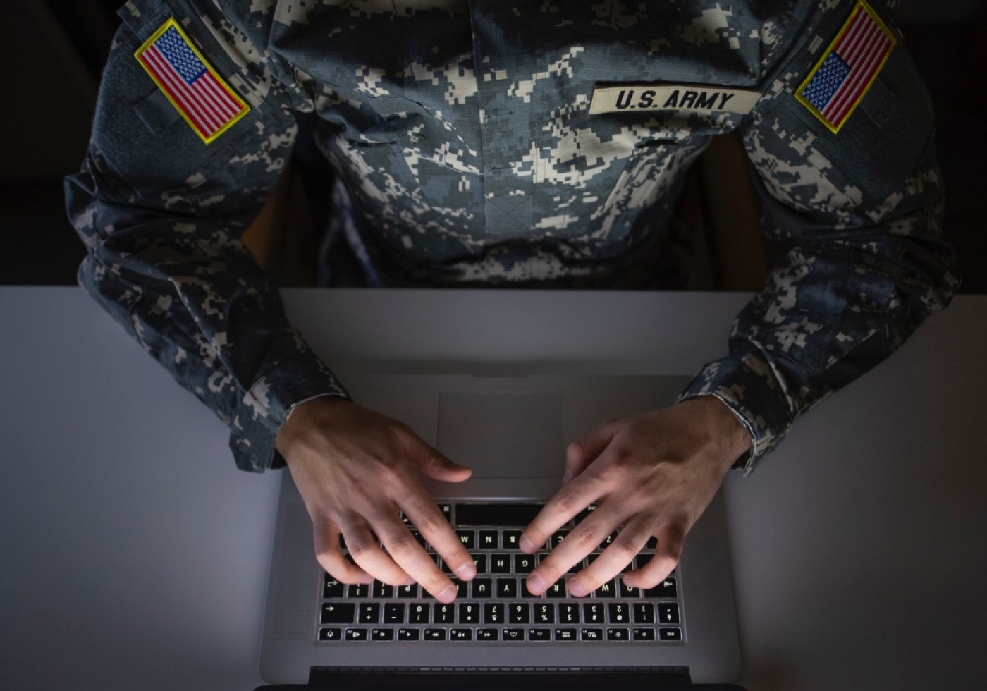 Soldier in U.S. Army uniform typing on a laptop, with hands visible on the keyboard.