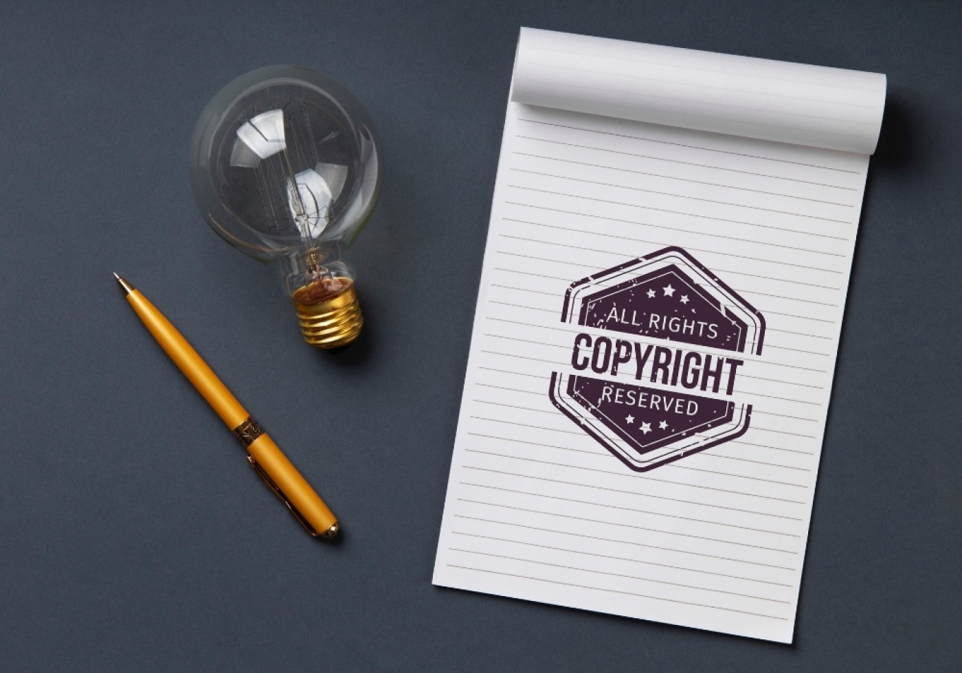 Notepad with 'Copyright Reserved' stamp, a light bulb, and a gold pen.