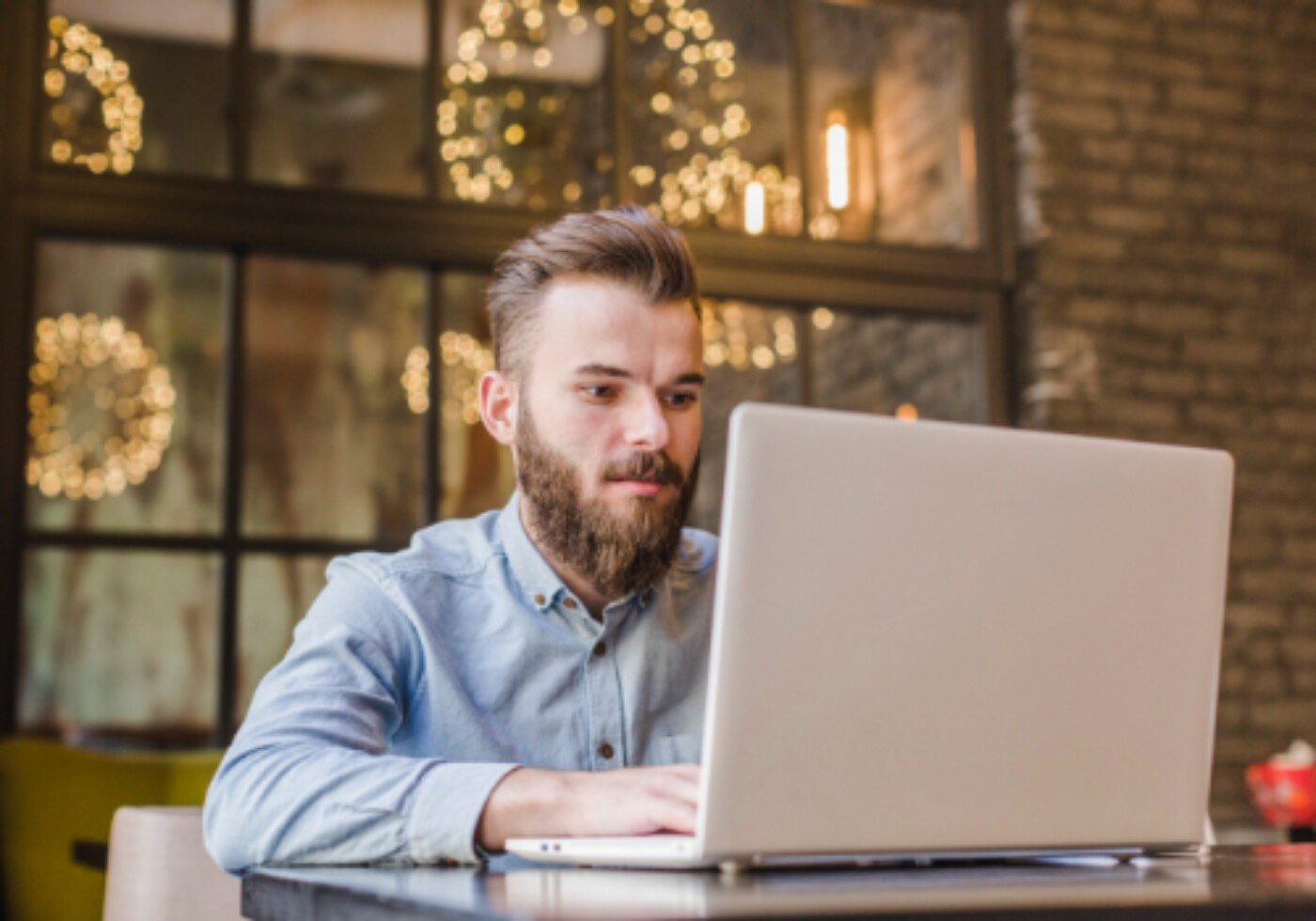 Man with a beard working on a laptop in a cozy, decorated cafe.