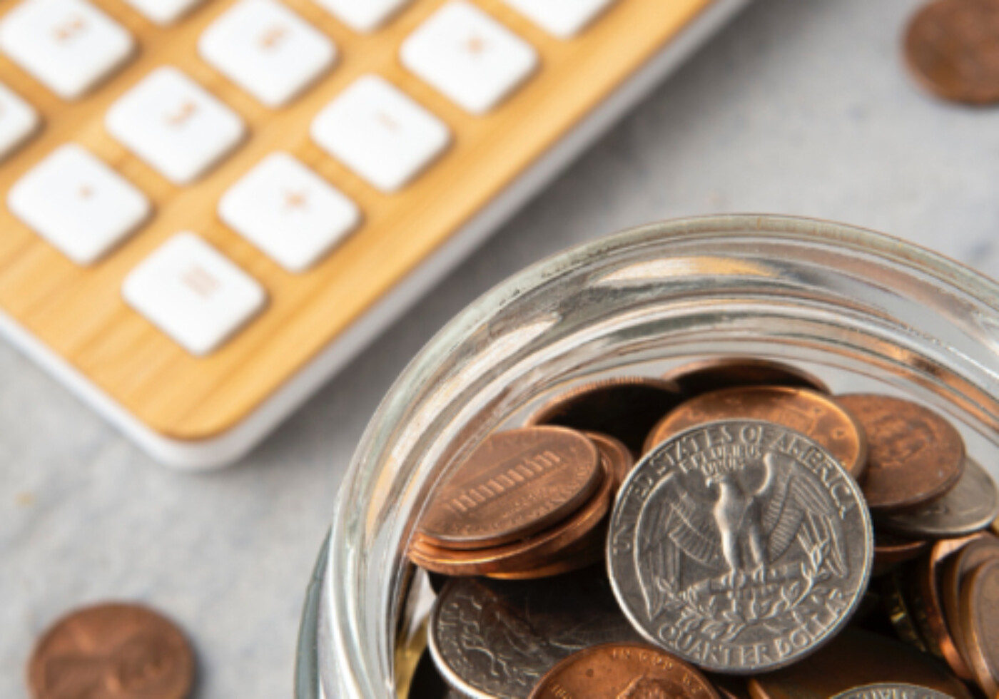 Jar of coins beside a calculator on a desk.