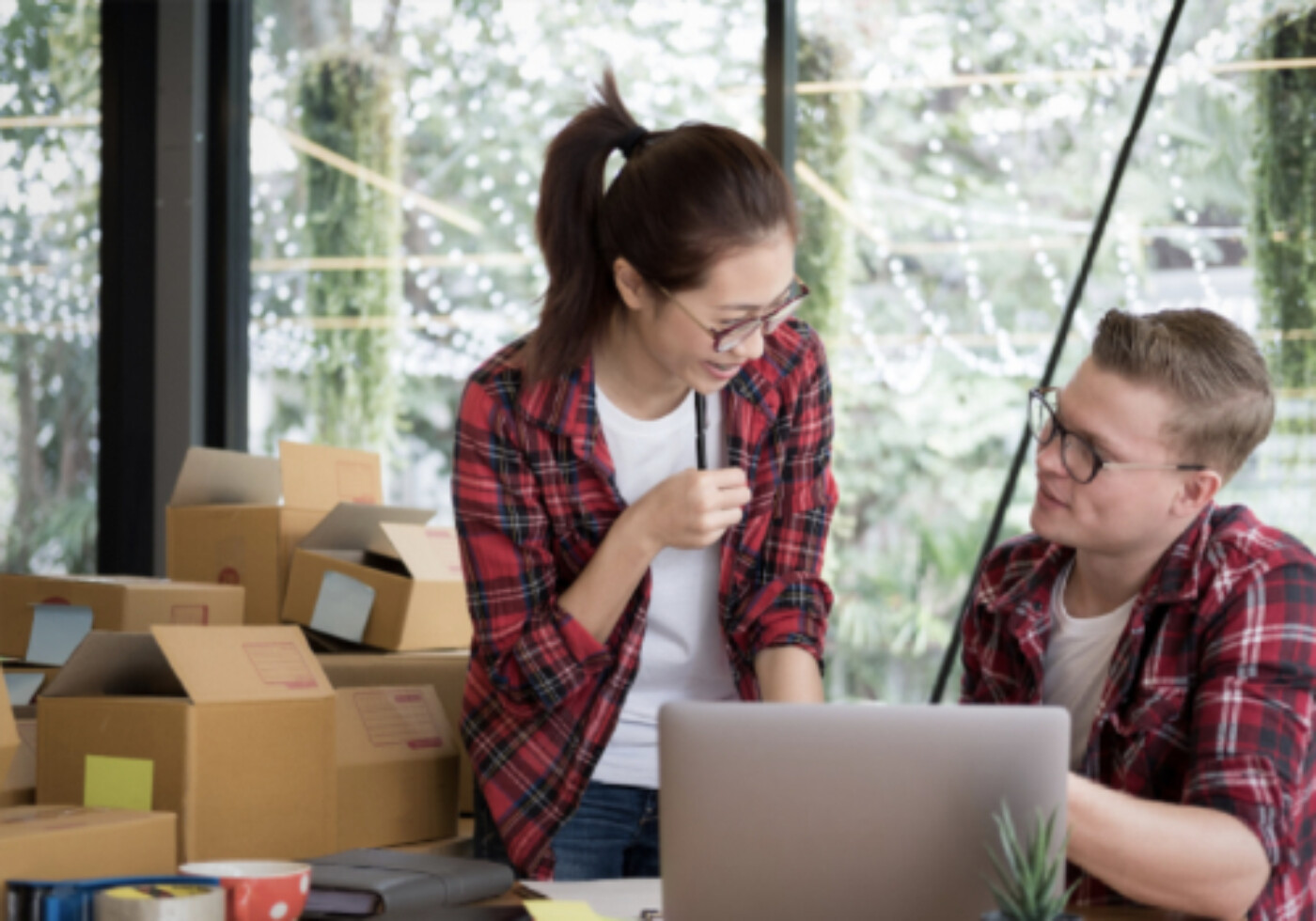 Two colleagues discussing work in a packaging area with boxes and a laptop.