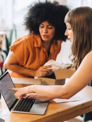 Two women discussing work at a table with a laptop and a package