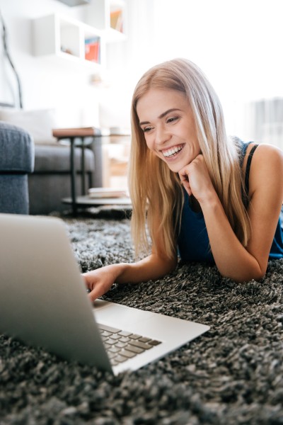 Woman smiling while using laptop on carpet.